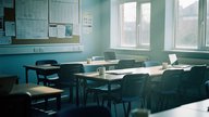 A quiet UK primary or secondary school staffroom in the early morning before pupils arrive, rows of empty desks and chairs, a noticeboard with paper timetables pinned to it, soft daylight through tall