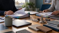 A small UK office meeting room in late afternoon, soft window light falling across printed supplier tender packs with coloured tab dividers, two closed laptops and neatly arranged sample components aw